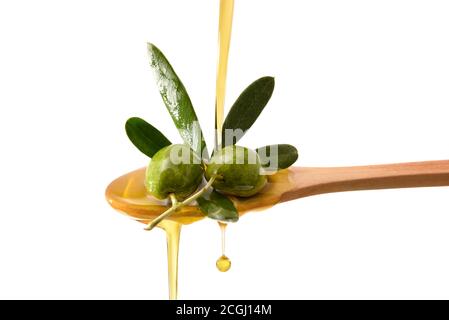 Olive oil falling on wooden spoon with raw olives with olive leaves with isolated white background. Stock Photo