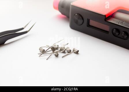 E-cigarette coils on a white background. Metal components for VAPE, consumables. Part of the VAPE and tweezers next to it. Stock Photo