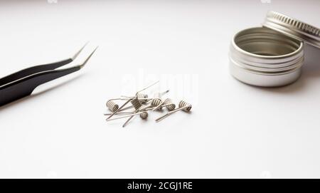 E-cigarette coils on a white background. Metal components for VAPE, consumables. Tweezers and a metal storage jar are next to each other. Stock Photo