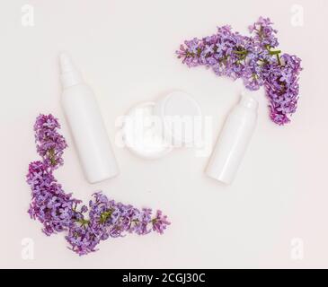 Cream in white bottles and a jar on a white background and lilac flowers. Skin care, health care, spa Stock Photo