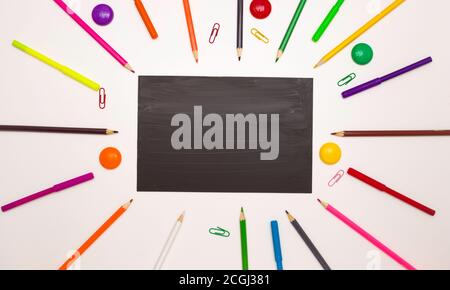 Background for school and student design. Colored pencils around a black rectangle. Free space for text. White background, top view. Stock Photo