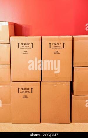 cardboard moving boxes stacked up against a red wall ready for transport Stock Photo