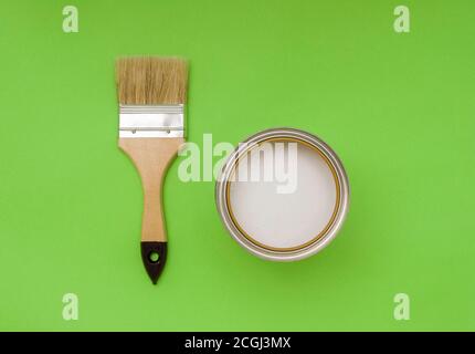 Tools for construction and decoration. Paintbrush next to a jar of white paint on a green background, top view. Stock Photo