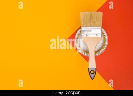 Concept of painting works. Paintbrush on a can of paint, yellow-red bright background, top view. Stock Photo