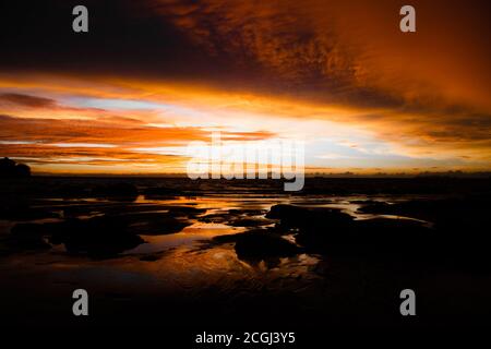 View from tropical beach over stones on dramatic orange yellow sunset over andaman sea with storm clouds, ko lanta, Thailand (focus on horizon) Stock Photo