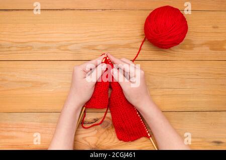 Women's hands with knitting needles and a red ball of yarn on a wooden background. Stock Photo