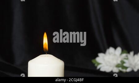 Condolence card. White memorial candle with white flowers in the background. Black background. Stock Photo