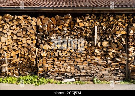chopped and cut beautiful brown firewood protected from rain and bad weather in storage under a brick roof, for a warm winter Stock Photo