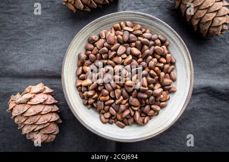 Cedar or pine nuts in a bowl with cones on gray background, top view Stock Photo