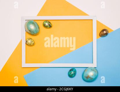 Colored Easter eggs around a wooden white frame on a white, yellow and blue background. Happy Easter! Stock Photo