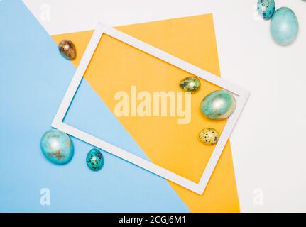 Colored Easter eggs around a wooden white frame on a white, yellow and blue background. Happy Easter! Stock Photo