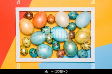 Colored Easter eggs in a wooden white frame on a colored background. Happy Easter! Stock Photo