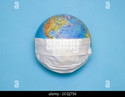 Disposable medical mask on the globe, model of the Earth. The concept of a pandemic. COVID-19, coronavirus. World epidemic of the disease. COVID Dange Stock Photo