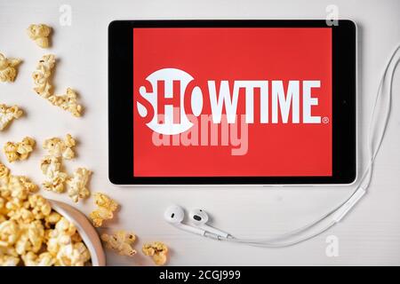 Showtime logo on the tablet screen laying on the white table with scattered popcorn and Apple earphones. Spending free time at home or news Stock Photo