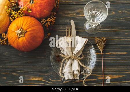 Eco friendly Thanksgiving dinner table setting. Stylish plate with cutlery, linen napkin with herb and pumpkin with autumn flowers on rustic table. Fa Stock Photo