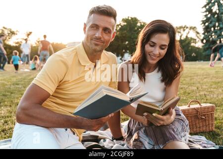 Portrait of pretty middle-aged couple man and woman smiling and reading books together during picnic in summer park Stock Photo