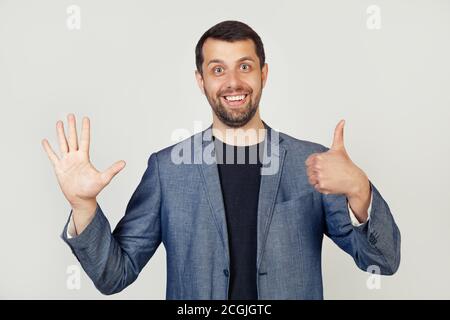 Young businessman man with beard smiling, showing number six with fingers on hand, smiling confidently and happily, looking into the camera. The man shows six fingers. Number 6. Stock Photo
