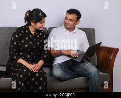 young Indian couple using the laptop sitting on a sofa. Stock Photo