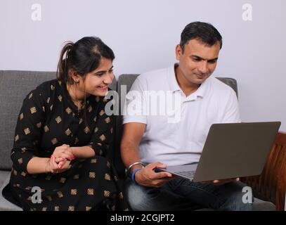 young Indian couple using the laptop sitting on a sofa. Stock Photo