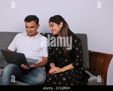 young Indian couple using the laptop sitting on a sofa. Stock Photo