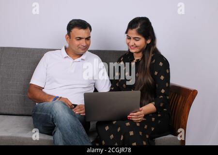 young Indian couple using the laptop sitting on a sofa. Stock Photo
