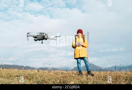Close up image of the flying drone with Teenager boy dressed yellow jacket on background piloting a modern digital drone using the remote controller Stock Photo
