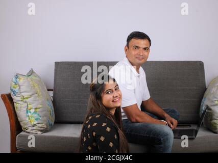 young Indian couple using the laptop sitting on a sofa. Stock Photo