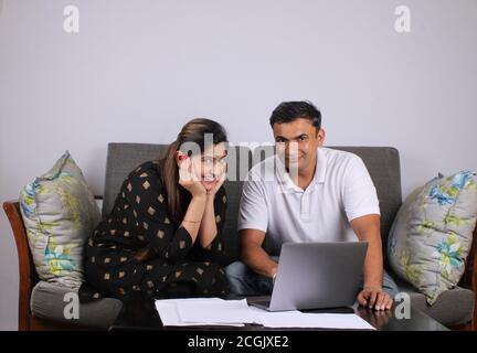young Indian couple using the laptop sitting on a sofa. Stock Photo