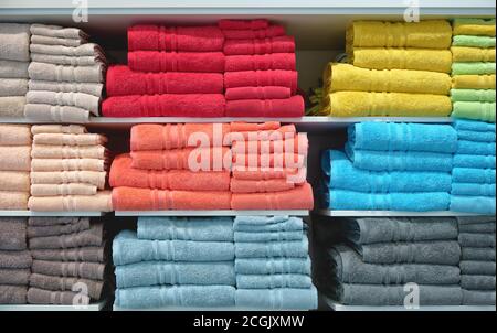 Stack of colorful fluffy bathing towels on shelf in shop, front view multicolored textile background Stock Photo