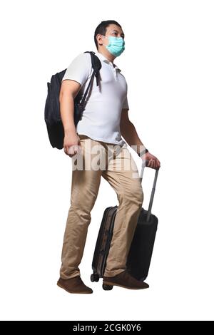 Asian man traveler with face mask walking drag his suitcase luggage during covid pandemic, wearing casual shirt and backpack, full length portrait iso Stock Photo