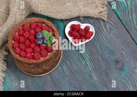No-bake chocolate cake with cream cheese. Garnished with raspberries, blueberries and mint leaves. On the surface of pine boards painted in black and Stock Photo