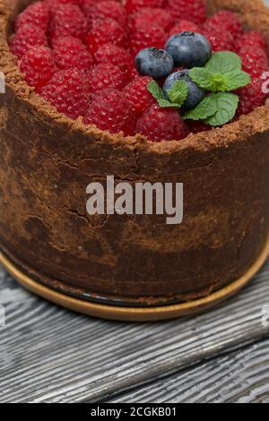 No-bake chocolate cake with cream cheese. Garnished with raspberries, blueberries and mint leaves. On the surface of pine boards painted in black and Stock Photo