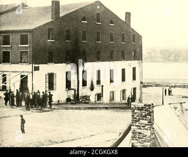. The photographic history of the Civil War : in ten volumes . LIBBY PRISON AFTER THE TABLES WERE TURNED In this dramatic record by the camera of April, 1865, appear Confederate captives pressing their faces against the bars through whichone hundred and twenty-five thousand Federal prisoners had gazed from the inside during the war. Union sentinels are guardingthe prison. Major Thomas P. Turner, who had been commandant of the prison, though a subordinate, Richard Turner, had moredirect authority, was confined here at this time. Strenuous efforts were made to secure evidence on whicli to prefer Stock Photo