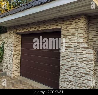 Automatic and convenient garage doors opening for a car with wall decore. Modern, plastic automatic roll-up and brown colored doorplastic, Stone Tiles Stock Photo
