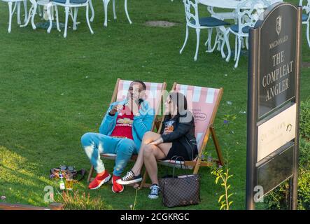 Young couple of different races enjoying a drink in a pub garden sitting in deckchairs, UK Stock Photo