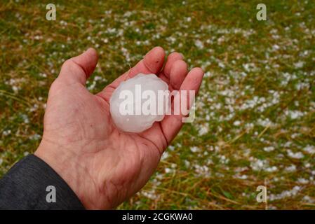 Person holding icy, hard, large, baseball size hail stone in cupped hand, weather made worse by climate change, Browntown, Wisconsin, USA Stock Photo