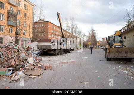 Public service workers put demolition waste of old pavilions in a truck with a crane in an alley near a residential building in the autumn. Stock Photo