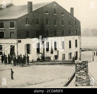 . The photographic history of the Civil War : thousands of scenes photographed 1861-65, with text by many special authorities . LIBBY PRISON AFTER THE TABLES WERE TURNED In this dramatic record by the camera of April, 1865, appear Confederate captives pressing their faces against the bars through whichone hmidred and twenty-five thousand Federal prisoners had gazed from the inside during the war. Union sentinels are guardingthe prison. Major Thomas P. Turner, who had been commandant of the prison, though a subordinate, Richard Turner, had moredirect authority, was confined here at this time. S Stock Photo