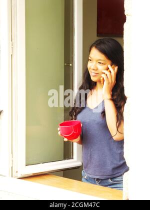 Close-up of an Afro-Asian woman on the phone at the window Stock Photo