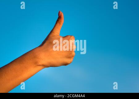 Female right hand giving thumb up like concept isolated on blue sky background. Stock Photo