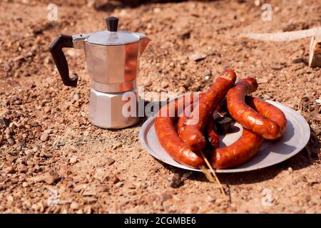 Geyser coffeemaker. Meat sausages are fried on a steel grilled grill against the backdrop of coals Stock Photo