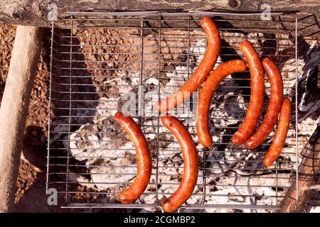 Meat sausages are fried on a steel grilled grill against the backdrop of coals Stock Photo