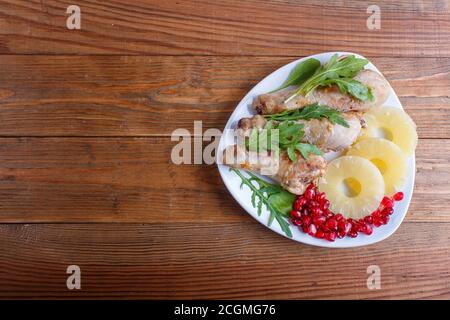 Fried chicken legs with rucola, pineapple and pomegranate seeds on brown wooden background, copy space, top view. Stock Photo