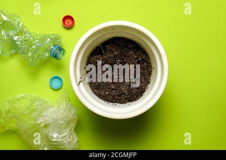 top view of pot with dead plant surrounded by bottles and plastic caps. ecology and recycling concept. flat lay flat design Stock Photo