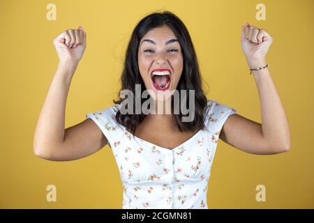 Beautiful woman over yellow background very happy and excited making winner gesture with raised arms, smiling and screaming for success. Stock Photo