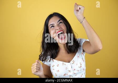 Beautiful woman over yellow background very happy and excited making winner gesture with raised arms, smiling and screaming for success. Stock Photo