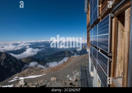 Solar panels mounted on the mountain refuge hut walls providing necessary electricity for a guest' needs with wide-angle Alps mountains landscape view Stock Photo