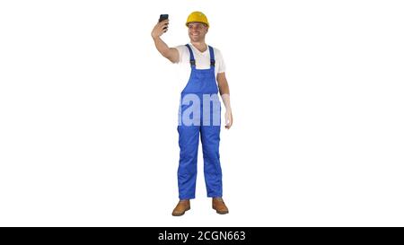 Smiling handsome young builder making selfie with mobile phone on white background. Stock Photo