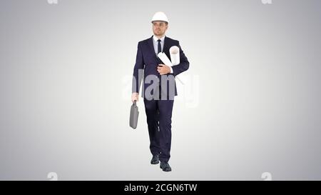 Male architect in a suit and hard hat walking with blueprints an Stock Photo