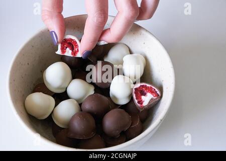 woman's hand choosing and grabbing fresh red and shiny fresh raspberries dipped in homemade black and white chocolate Stock Photo